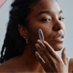 Young Black woman looking in the mirror with concern, wondering if the rash on her cheek is a lupus butterfly rash, rosacea, or eczema