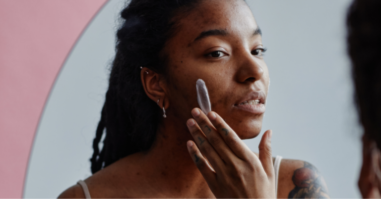 Battling Blood Cancers: Understanding the Disparities in Black Communities 1 Young Black woman looking in the mirror with concern, wondering if the rash on her cheek is a lupus butterfly rash, rosacea, or eczema